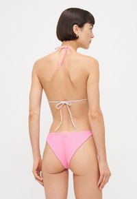 Roze bikini komplet s dizajnom na halter vrat i uzorkastim vezicama, od rebraste tkanine. Donji deo ima umereno visoki izrez.