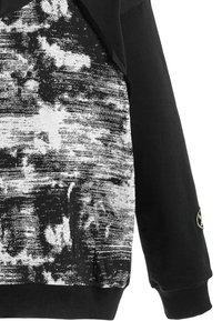 Sudadera negra con un patrón abstracto en blanco y gris texturizado en el frente, con puños y dobladillo acanalados y un parche con el logo en la manga.