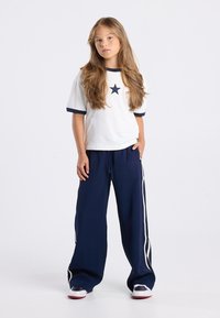 White T-shirt with navy trim and star graphic, paired with navy track pants featuring white side stripes, relaxed fit, and soft texture.