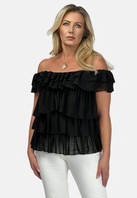 Czarny top bez ramiączek z warstwowymi falbanami, wykonany z lekkiego materiału z przezroczystą dolną częścią. Połączony z białymi spodniami.