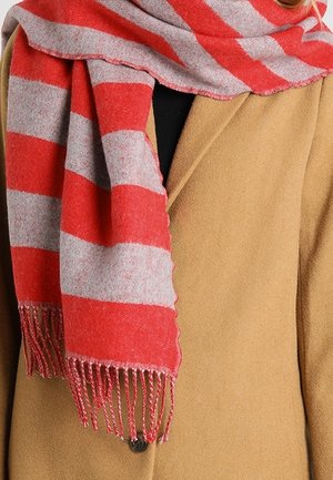 Écharpe rayée rouge et grise avec des franges drapée sur un manteau couleur chameau avec un bouton noir visible.