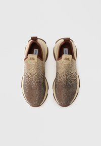 Pāris slip-on stila sporta apavu ar brūnu un bēšu gradientu, klāti maziem rhinestone akmentiņiem uz bēšiem zole, skatīts no augšas.