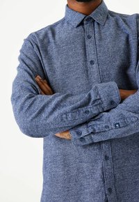 Modrá košile na knoflíky z texturované látky, s špičatým límcem a dlouhými rukávy se zapínáním na knoflíky. Logo na manžetě.