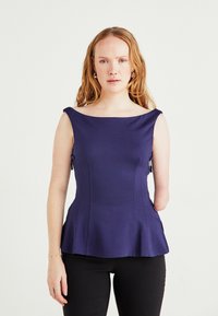 Ναυτικής μπλε τοπ με peplum σε λεία ύφανση, με φαρδύ λαιμό, πλαϊνές φερμουάρ και δομημένες ραφές. Μαύροι εφαρμοστοί παντελόνες ολοκληρώνουν την εμφάνιση.