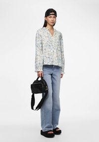 Gėlėta ilgomis rankovėmis marškiniai su šviesiai mėlynomis ir geltonomis raštais, derinami su šviesiai mėlynomis džinsais ir juodomis sandalais. Juoda rankinė per petį.