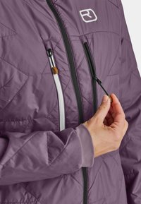 Purple quilted jacket with black zippers, white accents, and a hand adjusting the zipper. Features a smooth texture and fitted cuffs.