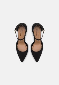 Ballerines noires à bout pointu avec bride à la cheville et semelles intérieures beige portant les inscriptions "Call It Spring" et "Vegan", vues de dessus sur un fond blanc.