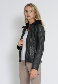 Schwarze Lederjacke mit einer gefütterten Kapuze aus schwarzem Stoff, Reißverschluss vorne, seitlichen Taschen und gerippten Akzenten an den Bündchen und am Saum.