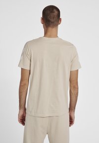 Lys beige bomulds T-shirt med korte ærmer, med hvide skulderdetaljer og en lige kant. Tekstureret, blød finish.