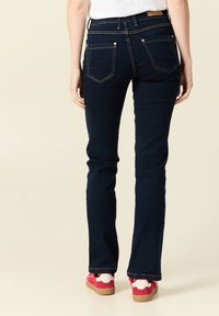 Ciemnoniebieskie dżinsy typu dzwony z widocznymi szwami, dwoma tylnymi kieszeniami i metką na pasku. Noszone z czerwono-białymi trampkami.