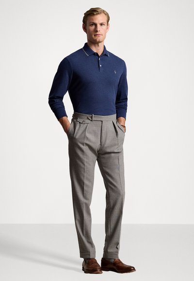 Jūras spēku polo krekls ar garām piedurknēm, pelēkas plisētās bikses un brūni ādas apavi. Iekļauj ribotu apkakli un pieguļošu piegriezumu.