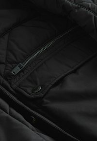 Černá podšitá bunda s podšívkou a zapínáním na zip s knoflíkem. Má prošívanou texturu a hladkou látkovou podšívku.