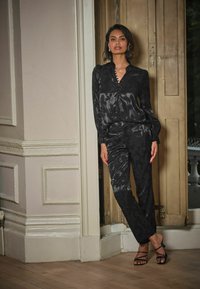 Black satin outfit featuring a textured floral pattern, a buttoned blouse with puffed sleeves, and straight-leg pants, paired with strappy sandals.