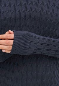 Maglione blu navy con un motivo a trecce testurizzato, polsini a costine e maniche attillate, che presenta un aspetto morbido e caldo.