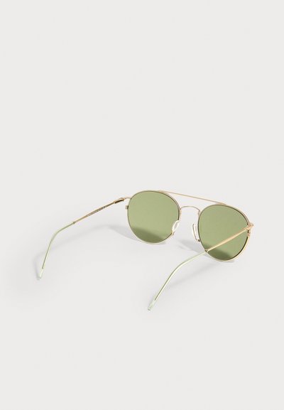 Γυαλιά ηλίου aviator με μεταλλικό σκελετό, φακούς με πράσινη απόχρωση και λεπτές ανοιχτοπράσινες άκρες στα μπράτσα, που ακουμπούν σε λευκή επιφάνεια.