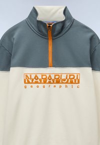 Half-zip pullover in cream and gray, featuring an orange embroidered logo. Soft fabric with a textured collar and contrasting upper section.