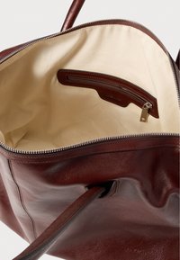 Brązowa skórzana torba typu tote z kremowym wnętrzem. Posiada kieszeń na suwak, plecione ozdoby oraz metalowy zamek. Miękka w dotyku i pojemna.