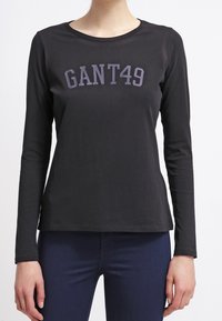 Musta pitkähihaisen t-paita, joka on valmistettu puuvillasta, ympyräkaula-aukolla ja rinnan kohdalla tummanharmaalla painatuksella "GANT49". Tiukka malli.