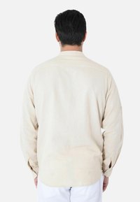 Camicia beige a maniche lunghe con colletto a punta, polsini abbottonati e vestibilità rilassata, realizzata in tessuto leggero, con yoke sul retro.