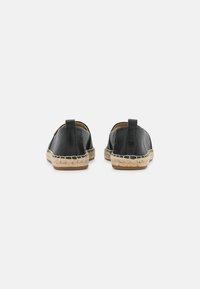 Zapatos negros de cuero sin cordones con una suela de yute trenzado y un acabado texturizado. Cuentan con un pequeño tacón y una pestaña trasera para facilitar su uso.