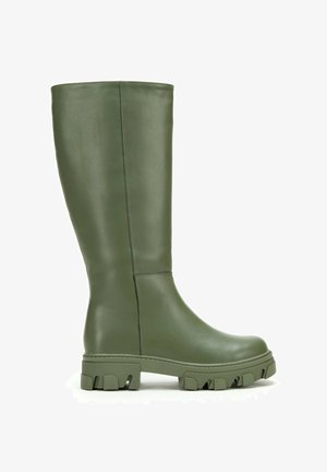 Wysoki oliwkowozielony skórzany but z grubą, bieżnikowaną podeszwą i gładką cholewką, widok z boku na białym tle.