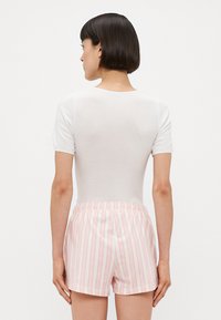 Vit kortärmad topp i kombination med rosa shorts som har vertikala vita och persikofärgade ränder. Shortsen har en elastisk midja.
