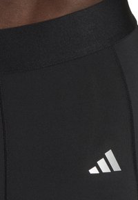 Schwarze Sportleggings haben eine glatte, dehnbare Textur mit einem breiten Bund und einem silbernen Adidas-Logo unten links.