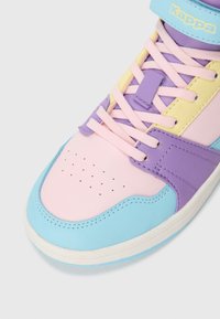 Lähedalne vaade värvilisele tossule, millel on pastelltoonis sinine, roosa, kollane ja lilla paneel ning roosa seotud väikese kleeplindiga valge tausta peal.