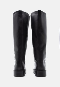 Czarne skórzane kozaki sięgające za kolano, o gładkiej powierzchni, z grubym obcasem i widocznym przeszyciem. Logo marki na zewnętrznej górnej części.