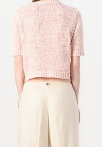 Rosa gestrickter, kurzärmeliger Cropped-Pullover mit strukturiertem und lockerer Webart. Kombiniert mit beigen, hoch taillierten Hosen mit einem Knopf-Detail.