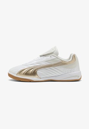 Zapatilla de fútbol sala blanca con raya lateral dorada, suela de goma, cuello acolchado y cubrecordones, sobre fondo blanco.