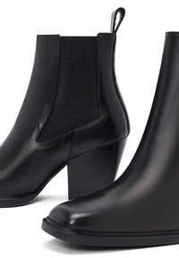 Botas de cuero negro hasta el tobillo con un acabado liso, paneles laterales elásticos y un tacón ancho, con punta redonda y tira de agarre.