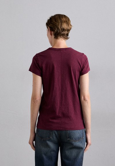 Bordeauxrotes T-Shirt mit kurzen Ärmeln, weicher Stoff, runder Halsausschnitt, gerader Schnitt, minimale Nähte, kombiniert mit weit geschnittenen blauen Jeans.