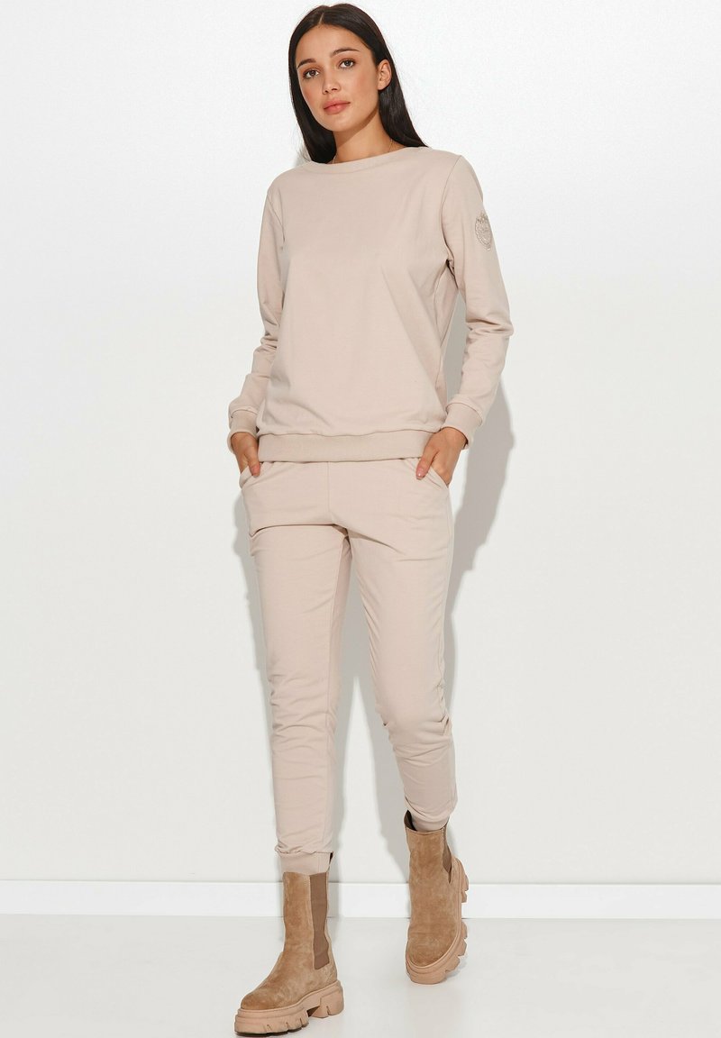 Beżowy zestaw bluzy i spodni dresowych wykonany z miękkiego materiału, z okrągłym dekoltem, ściągaczami na rękawach i bocznymi kieszeniami, zestawiony z brązowymi botkami za kostkę.