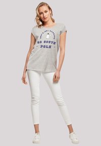 Graues kurzärmliges T-Shirt mit blauer Schrift "GO SOUTH POLE" und einer Pinguin-Grafik. Kombiniert mit weißen Skinny-Jeans und weißen Turnschuhen.