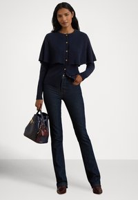 Tumesinine kootud kardigan kihilise kapuutsidisainiga, nööpidega kinnitatav, kombineeritud tumedate teksade ja kahvatu kahetoonilise käekotiga. Tekstuuriga kangas ja keha ümbritsev siluett.