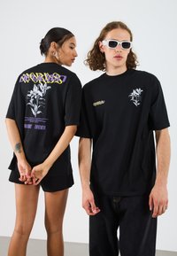 Black oversized t-shirts feature white floral graphics and text on the back, with one wearing white sunglasses and the other with a tattoo.