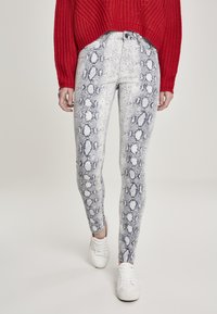 Jean skinny avec un motif serpent dans des nuances de gris et de bleu, associé à un pull en tricot rouge et des baskets blanches.