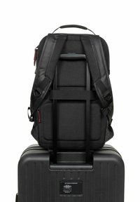 Black backpack with padded straps and mesh panels, secured on a black hard shell suitcase with a retractable handle.