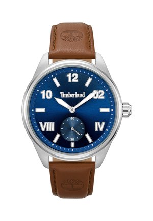 Zegarek na brązowym skórzanym pasku z stalową kopertą, niebieską tarczą, srebrnymi znacznikami godzinowymi i sub-tarczą na pozycjonowaniu 6. godziny.