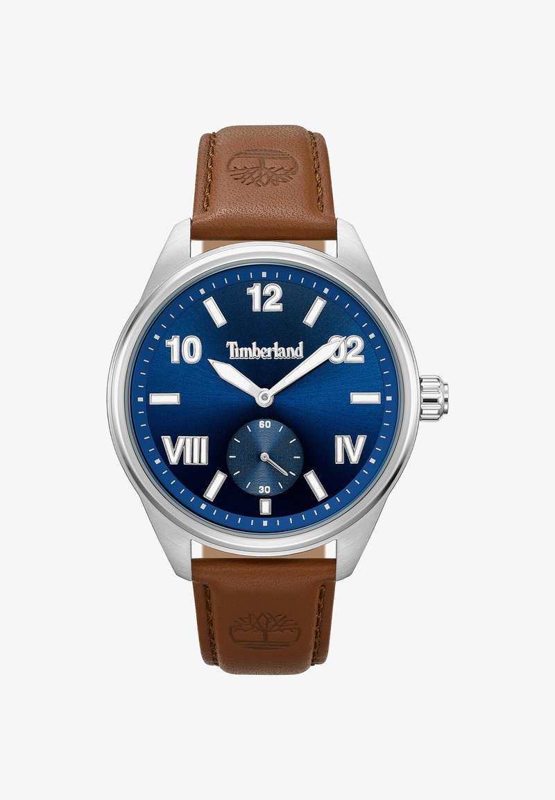 Zegarek na brązowym skórzanym pasku z stalową kopertą, niebieską tarczą, srebrnymi znacznikami godzinowymi i sub-tarczą na pozycjonowaniu 6. godziny.