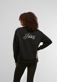 Črna dukserica z napisom "Juicy" v rhinestones na hrbtni strani. Ima ohlapen kroj, dolge rokave ter rebrast rob in manšete.