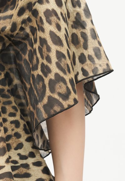 Διαφανές ύφασμα με τύπωμα λεοπάρδαλης και μαύρη επένδυση που κρέμεται πάνω από γυμνό χέρι μπροστά σε λευκό φόντο.