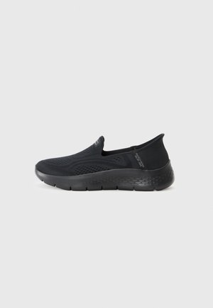 Zapatos negros tipo slip-on con parte superior de punto texturizado y suela acolchada, que presentan un diseño ligero y una marca mínima.