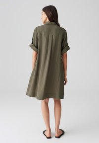 Abito verde oliva a maniche corte con un design testurizzato a coste. Presenta un colletto e una vestibilità morbida, che arriva a metà coscia. Orlo semplice, stile casual.