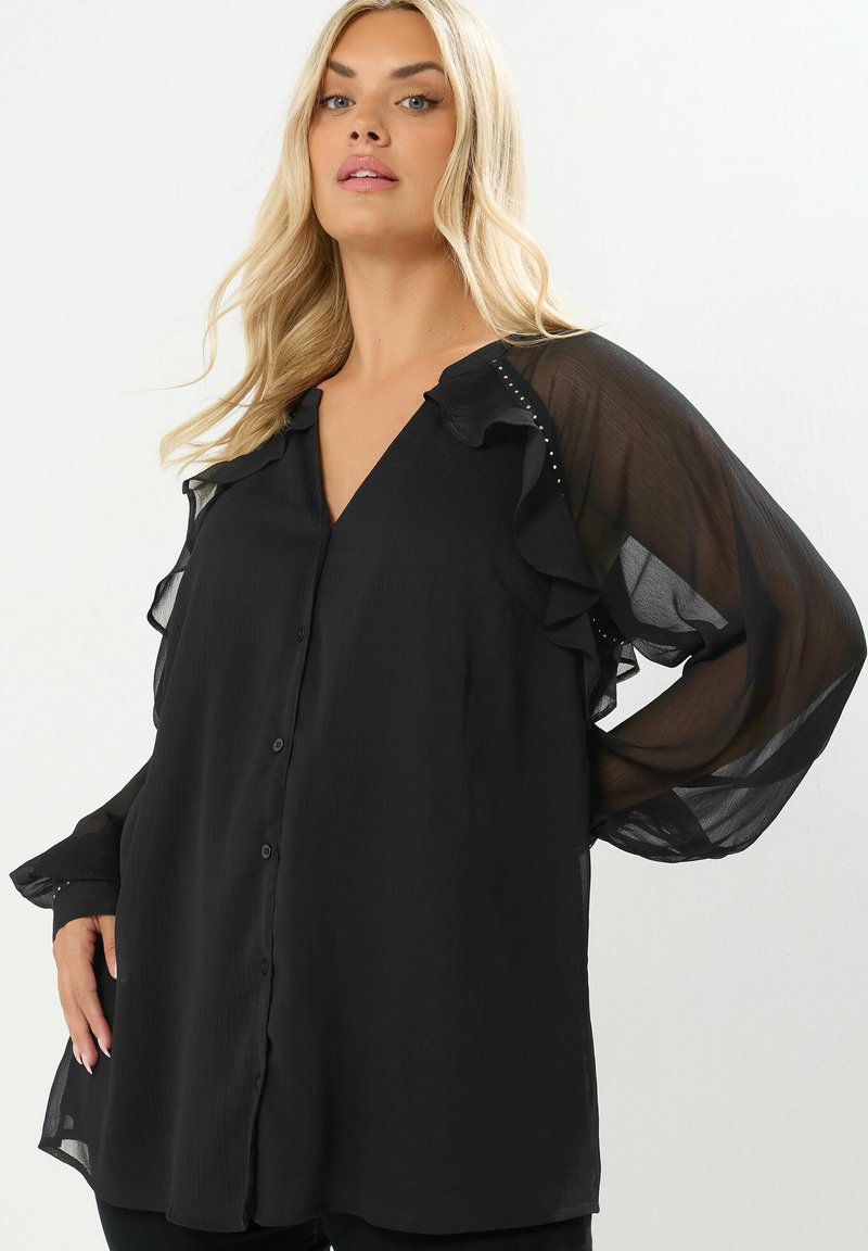 Blusa nera con maniche arricciate e scollo a V. Presenta bottoni sul davanti e delicati dettagli lungo le maniche. Tessuto sottile e trasparente.