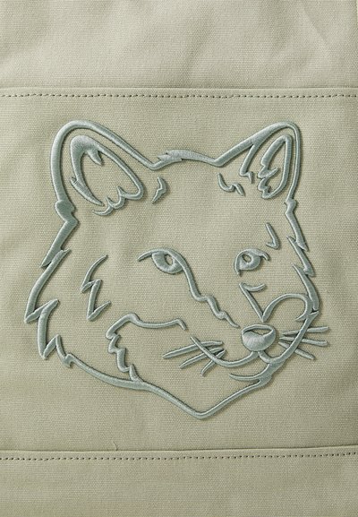La tela verde presenta un diseño bordado de la cabeza de un zorro en un tono más claro, mostrando líneas finas para los detalles faciales y los bigotes.