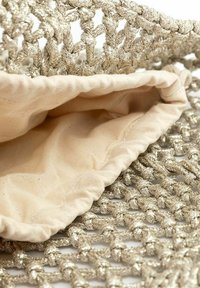 Sac tissé avec des fils dorés métalliques, doté d'une doublure intérieure beige. Le design comprend un motif noué et une ouverture froncée.