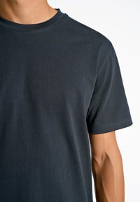 Tummansininen puuvillapaita, jossa on pyöreä pääntie ja lyhyet hihat. Paidassa on sileä pinta ja vähäiset ompeluyksityiskohdat.