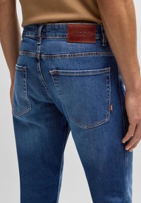 Donkerblauwe denim jeans met een soepele textuur, vijf zakken en een bruine leren taillebandlabel met de opdruk "BOSS."